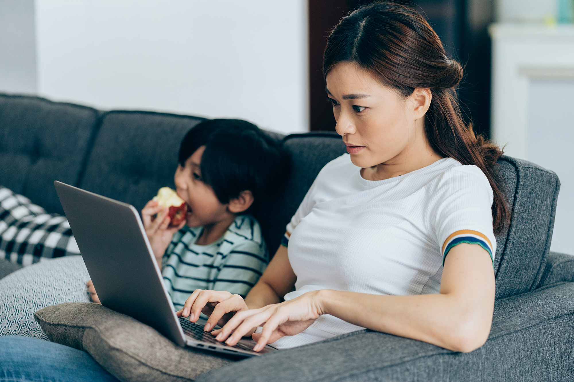 Mom taking online course with son sitting next to her from the comfort of her couch